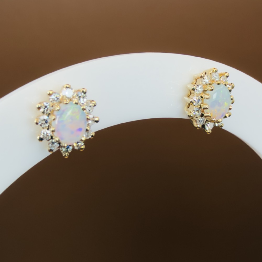 A pair of 9ct yellow gold stud earrings featuring central oval cabochon opals surrounded by a halo of small brilliant-cut diamonds. View XIII
