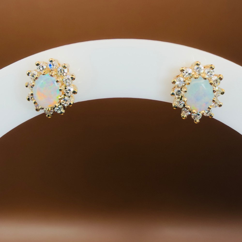 A pair of 9ct yellow gold stud earrings featuring central oval cabochon opals surrounded by a halo of small brilliant-cut diamonds.