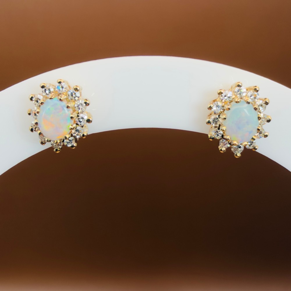 A pair of 9ct yellow gold stud earrings featuring central oval cabochon opals surrounded by a halo of small brilliant-cut diamonds. View XIV
