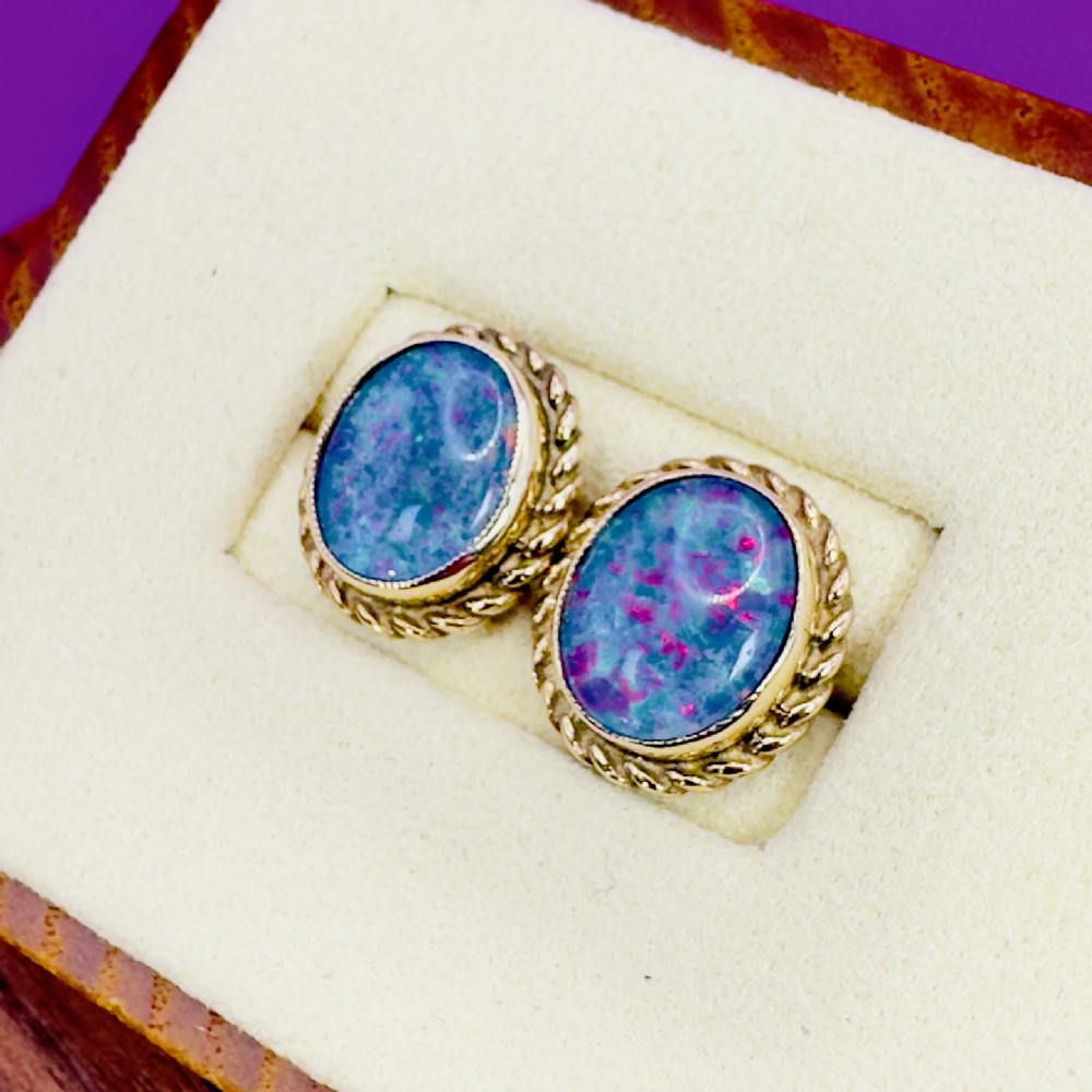 A pair of oval 9ct yellow gold stud earrings featuring iridescent black opal doublets surrounded by a twisted rope border. View IV