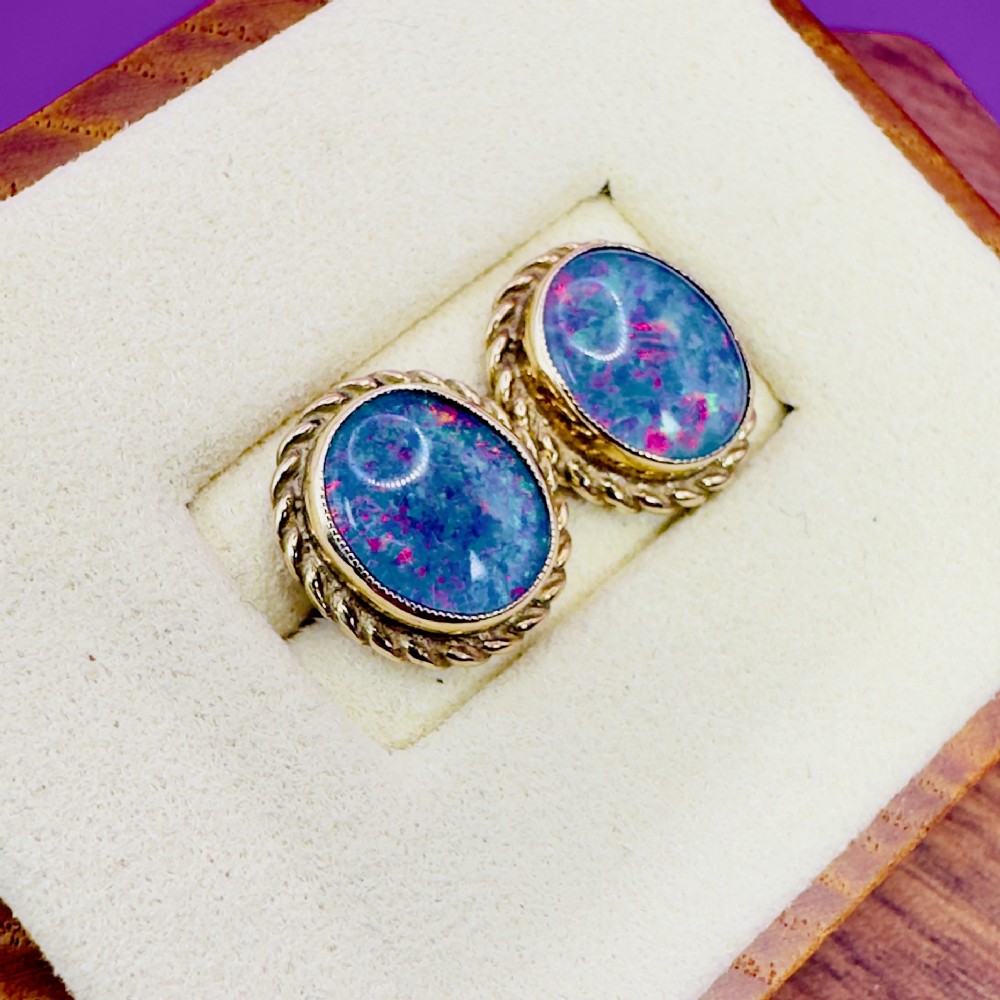 A pair of oval 9ct yellow gold stud earrings featuring iridescent black opal doublets surrounded by a twisted rope border. View V