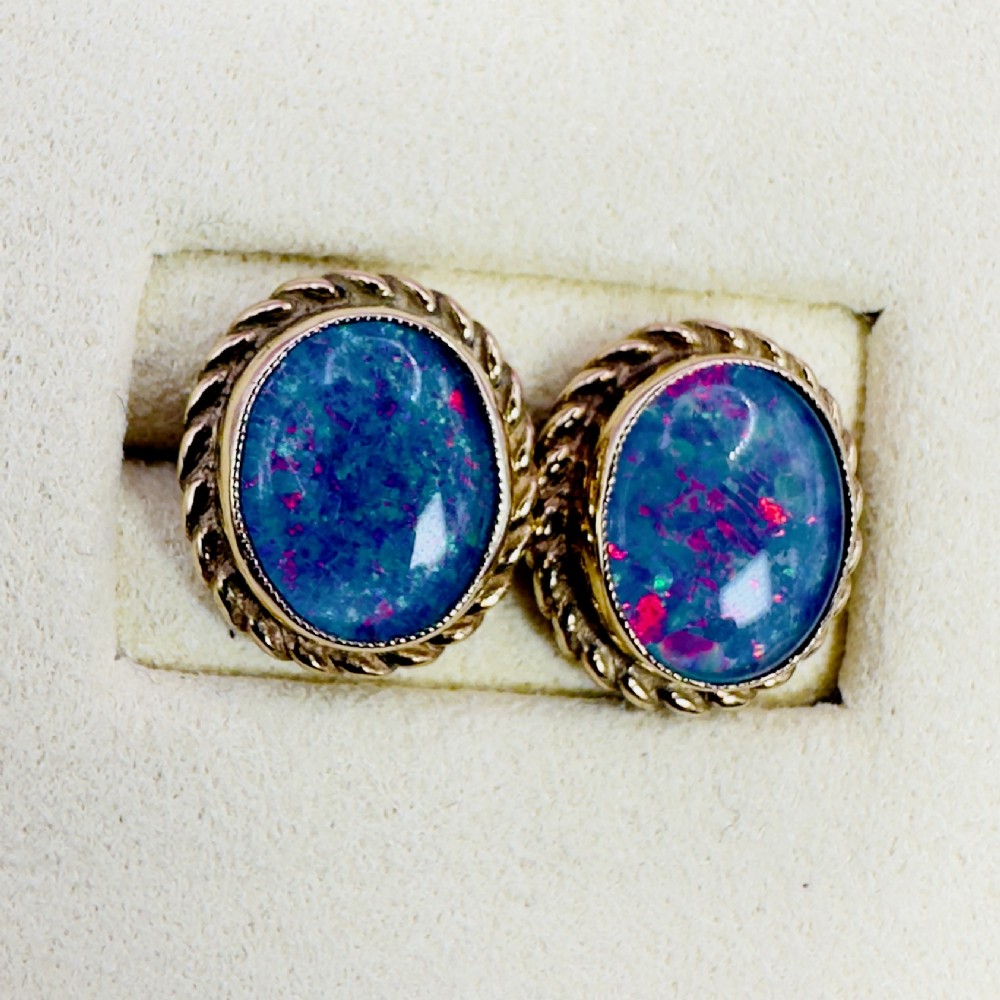A pair of oval 9ct yellow gold stud earrings featuring iridescent black opal doublets surrounded by a twisted rope border. View VI