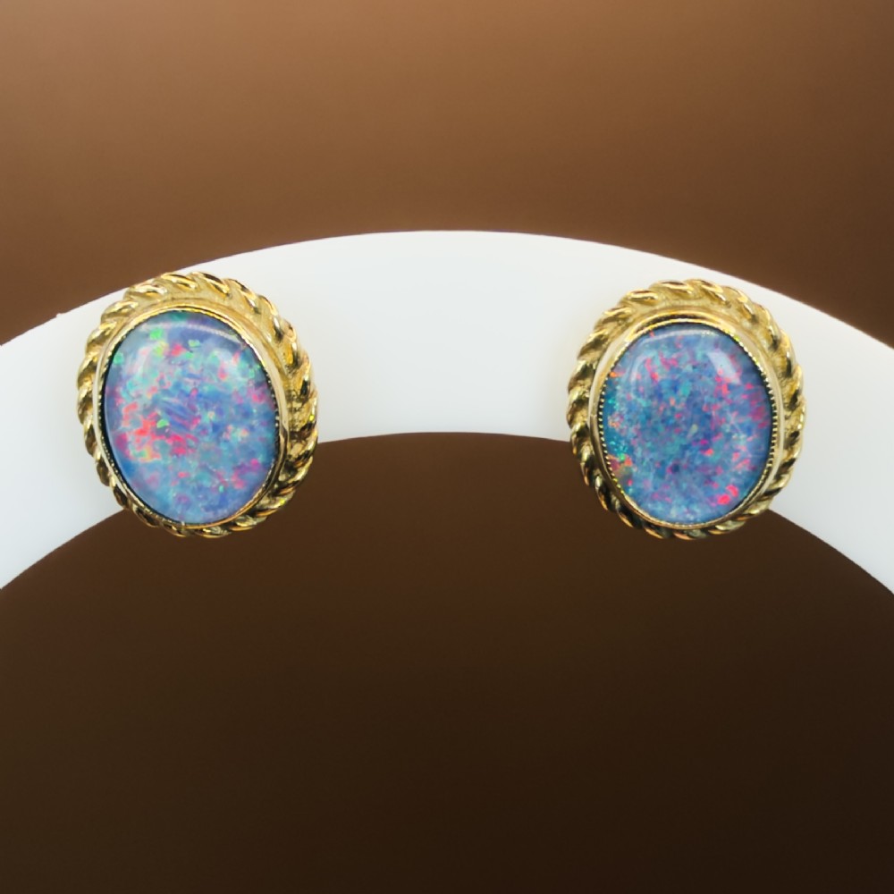 A pair of oval 9ct yellow gold stud earrings featuring iridescent black opal doublets surrounded by a twisted rope border. View VIII
