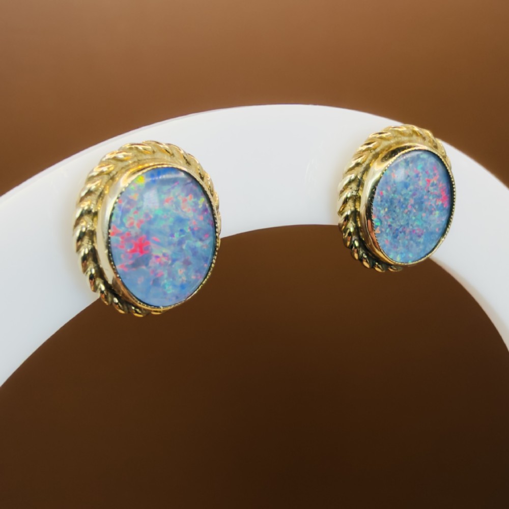 A pair of oval 9ct yellow gold stud earrings featuring iridescent black opal doublets surrounded by a twisted rope border. View IX