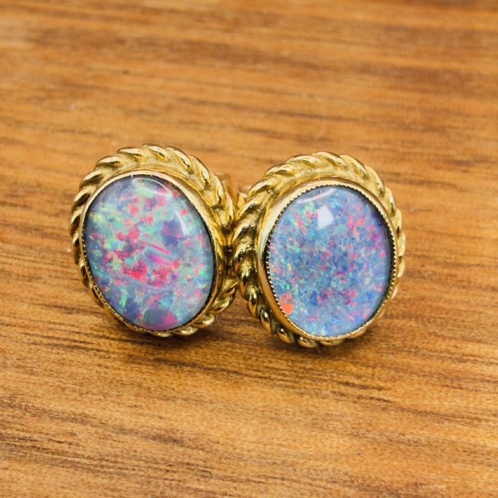 A pair of oval 9ct yellow gold stud earrings featuring iridescent black opal doublets surrounded by a twisted rope border. View II