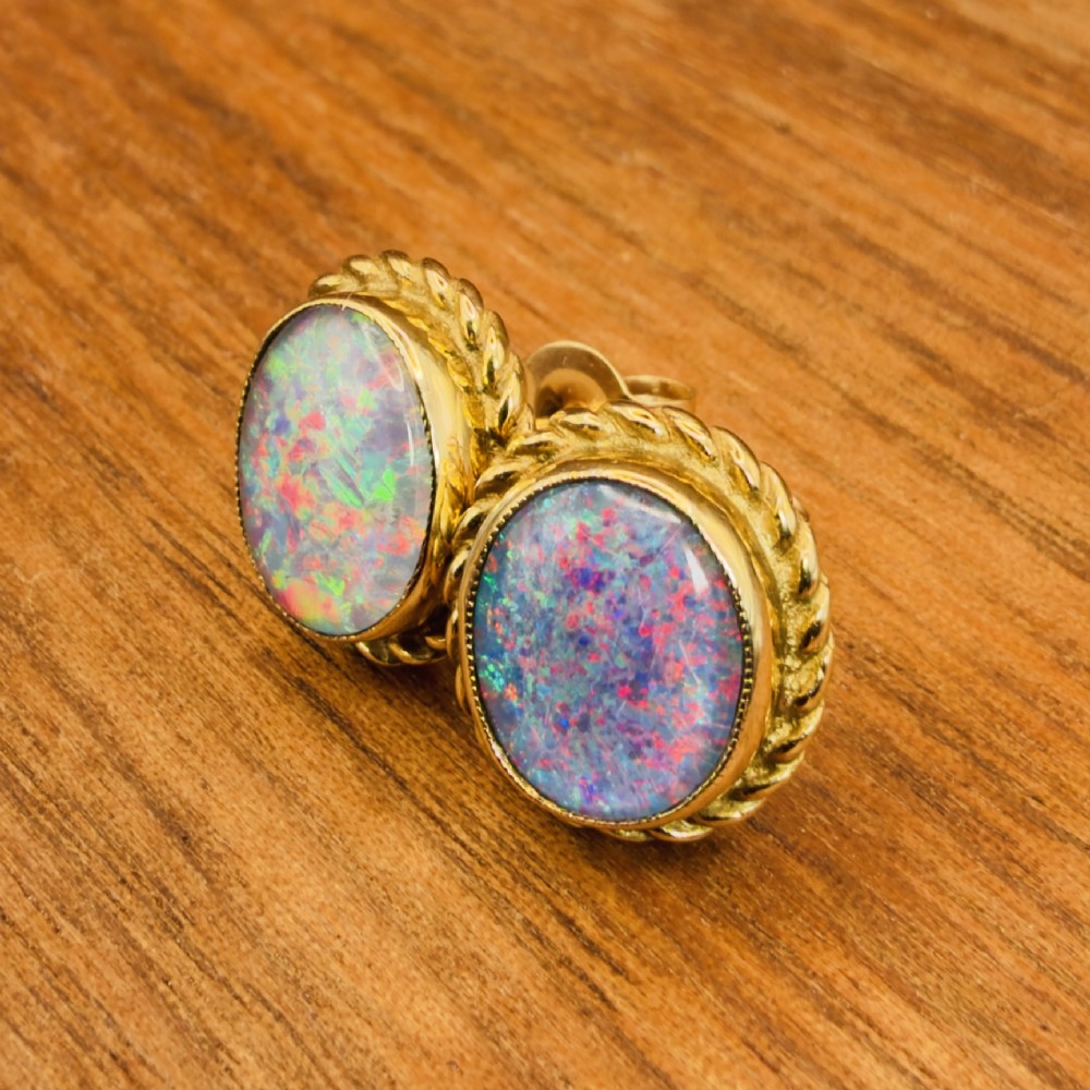 A pair of oval 9ct yellow gold stud earrings featuring iridescent black opal doublets surrounded by a twisted rope border. View X