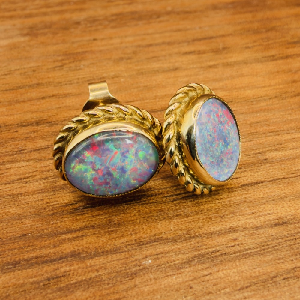 A pair of oval 9ct yellow gold stud earrings featuring iridescent black opal doublets surrounded by a twisted rope border. View XI