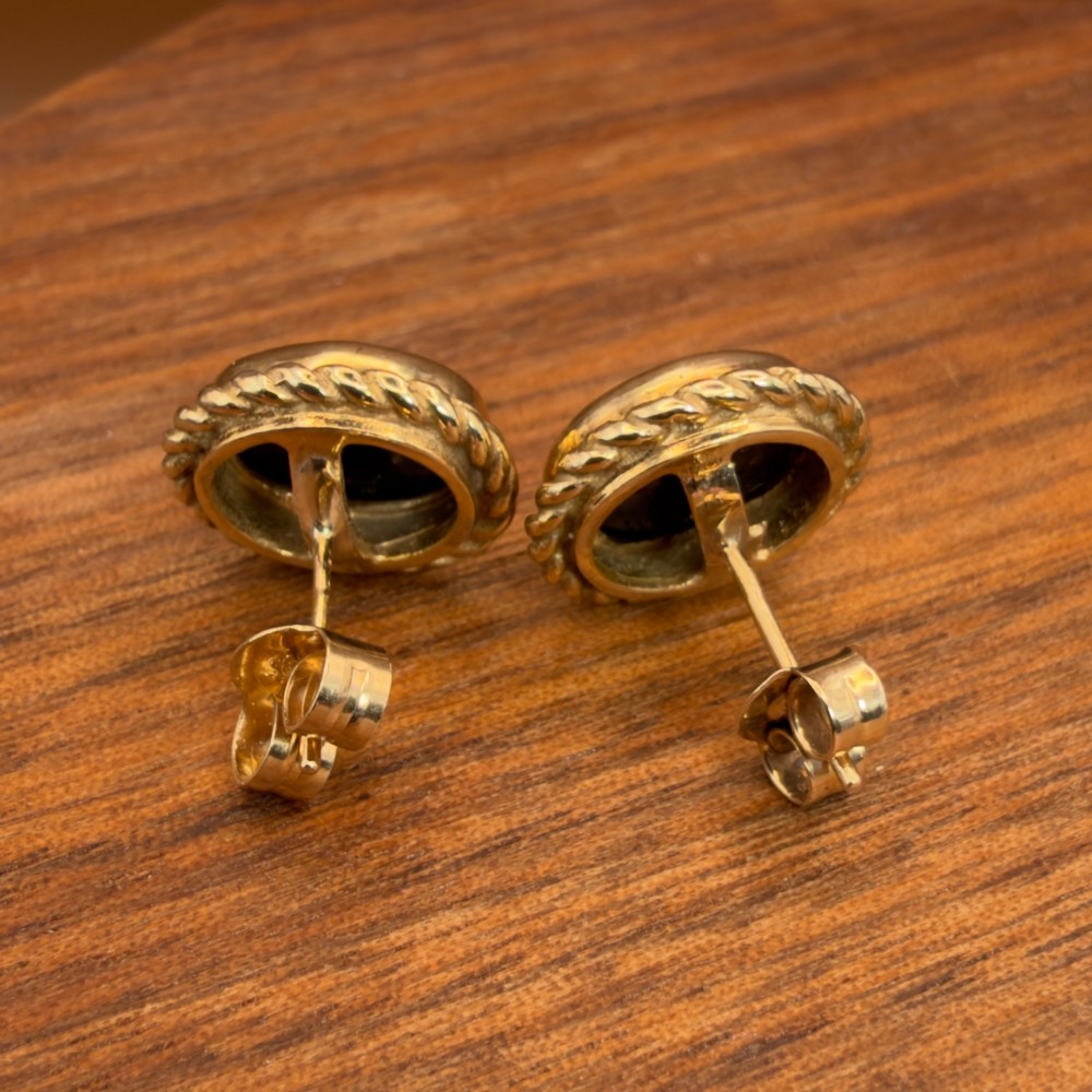A pair of oval 9ct yellow gold stud earrings featuring iridescent black opal doublets surrounded by a twisted rope border. View XII