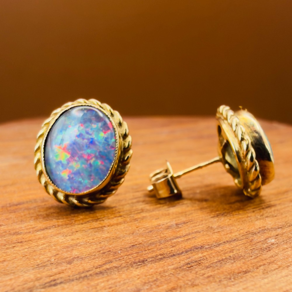 A pair of oval 9ct yellow gold stud earrings featuring iridescent black opal doublets surrounded by a twisted rope border. View XIII
