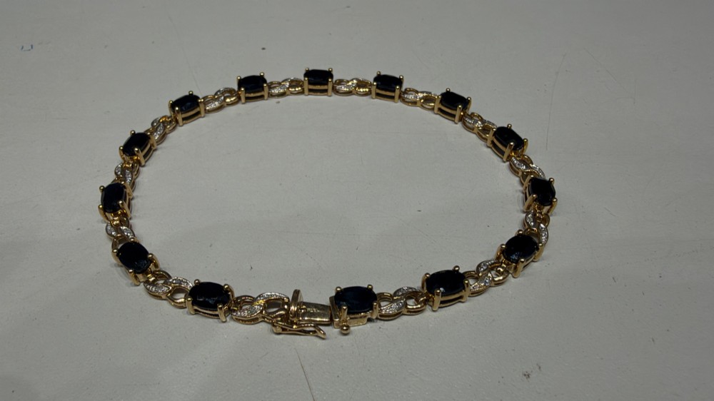 A 9ct yellow gold link bracelet set with oval-cut dark blue sapphires and accent diamond links, worn on a wrist. View XII