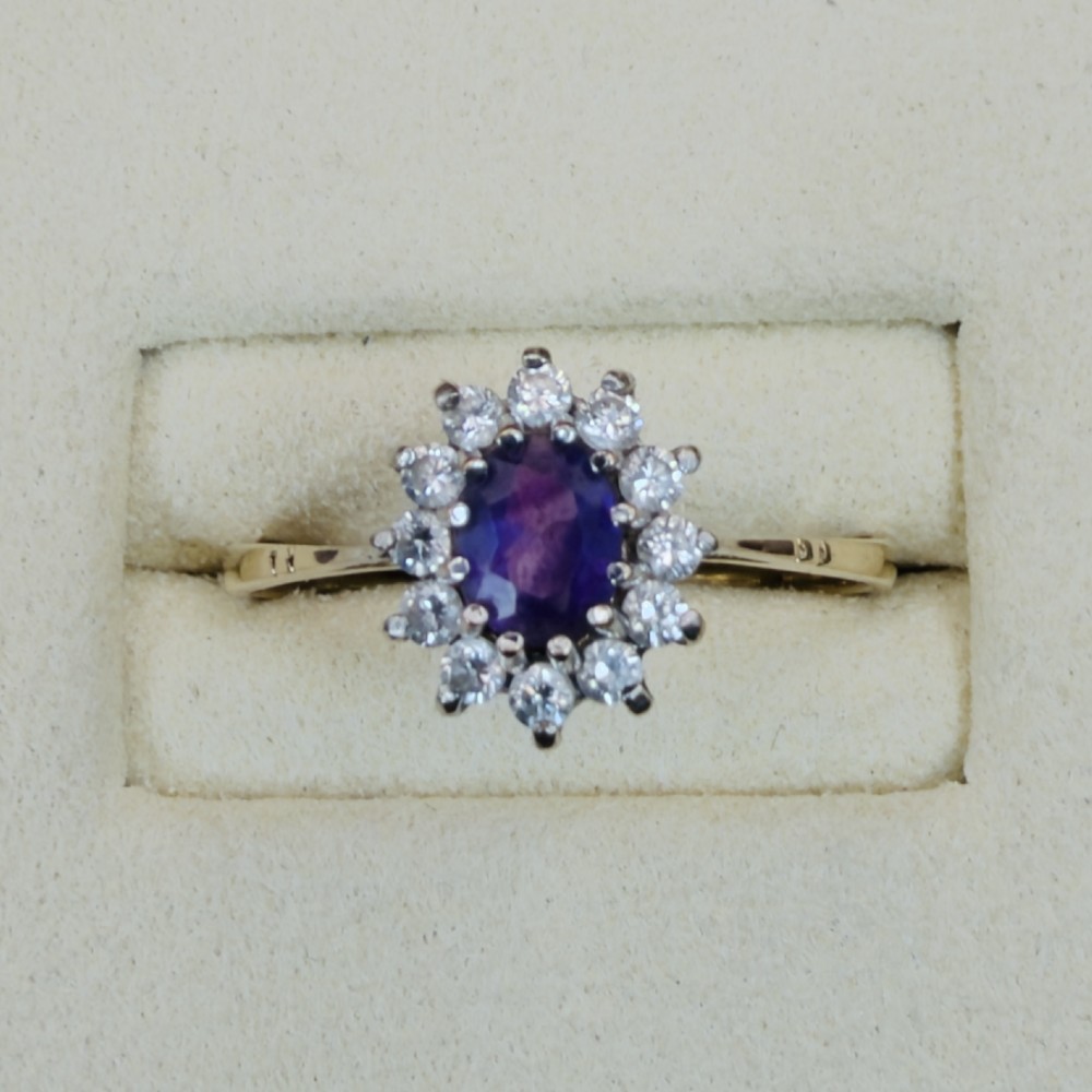 A vintage 9ct yellow gold ring featuring a central oval purple amethyst framed by a halo cluster of round white spinel gemstones. View II