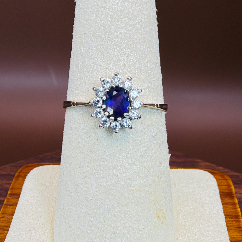 A vintage 9ct yellow gold ring featuring a central oval purple amethyst framed by a halo cluster of round white spinel gemstones. View V
