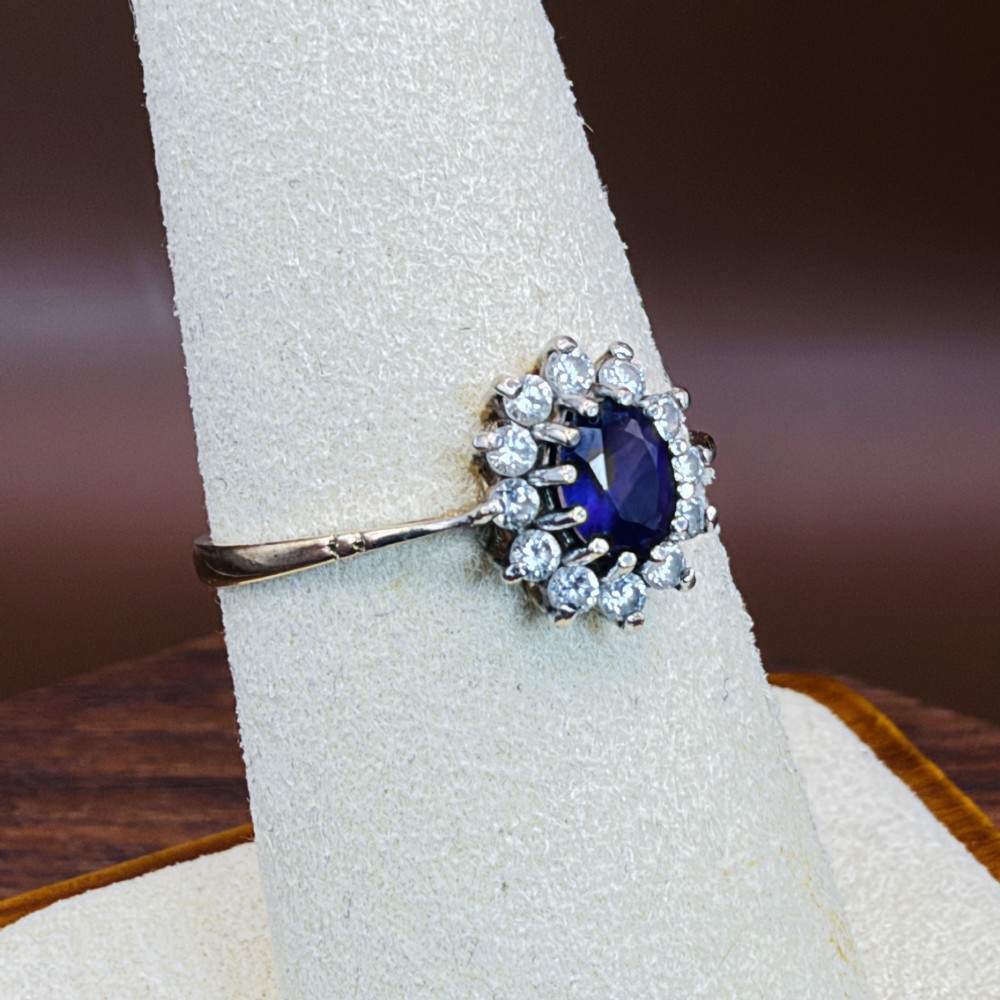 A vintage 9ct yellow gold ring featuring a central oval purple amethyst framed by a halo cluster of round white spinel gemstones. View VII