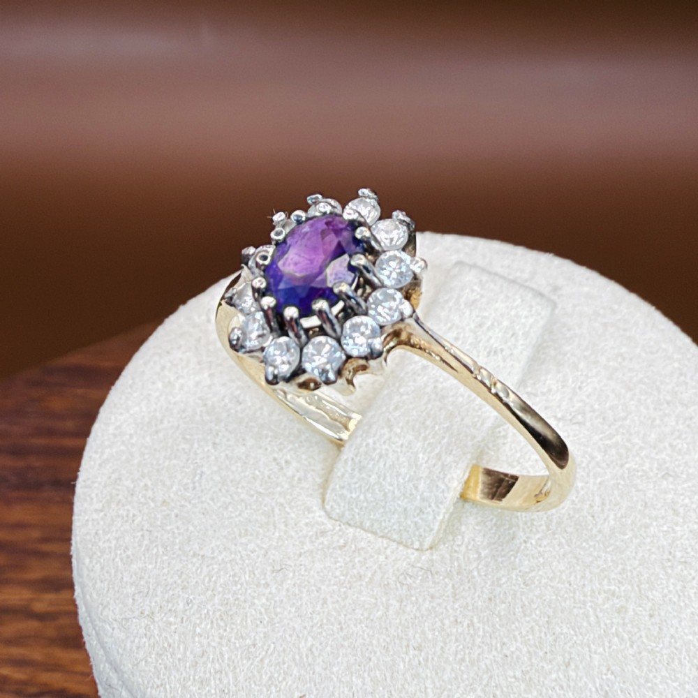 A vintage 9ct yellow gold ring featuring a central oval purple amethyst framed by a halo cluster of round white spinel gemstones. View XI