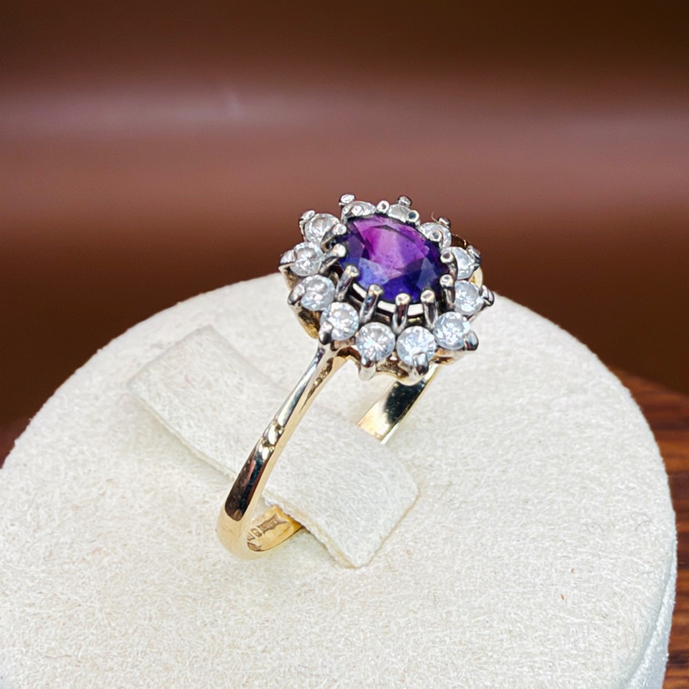 A vintage 9ct yellow gold ring featuring a central oval purple amethyst framed by a halo cluster of round white spinel gemstones. View XII