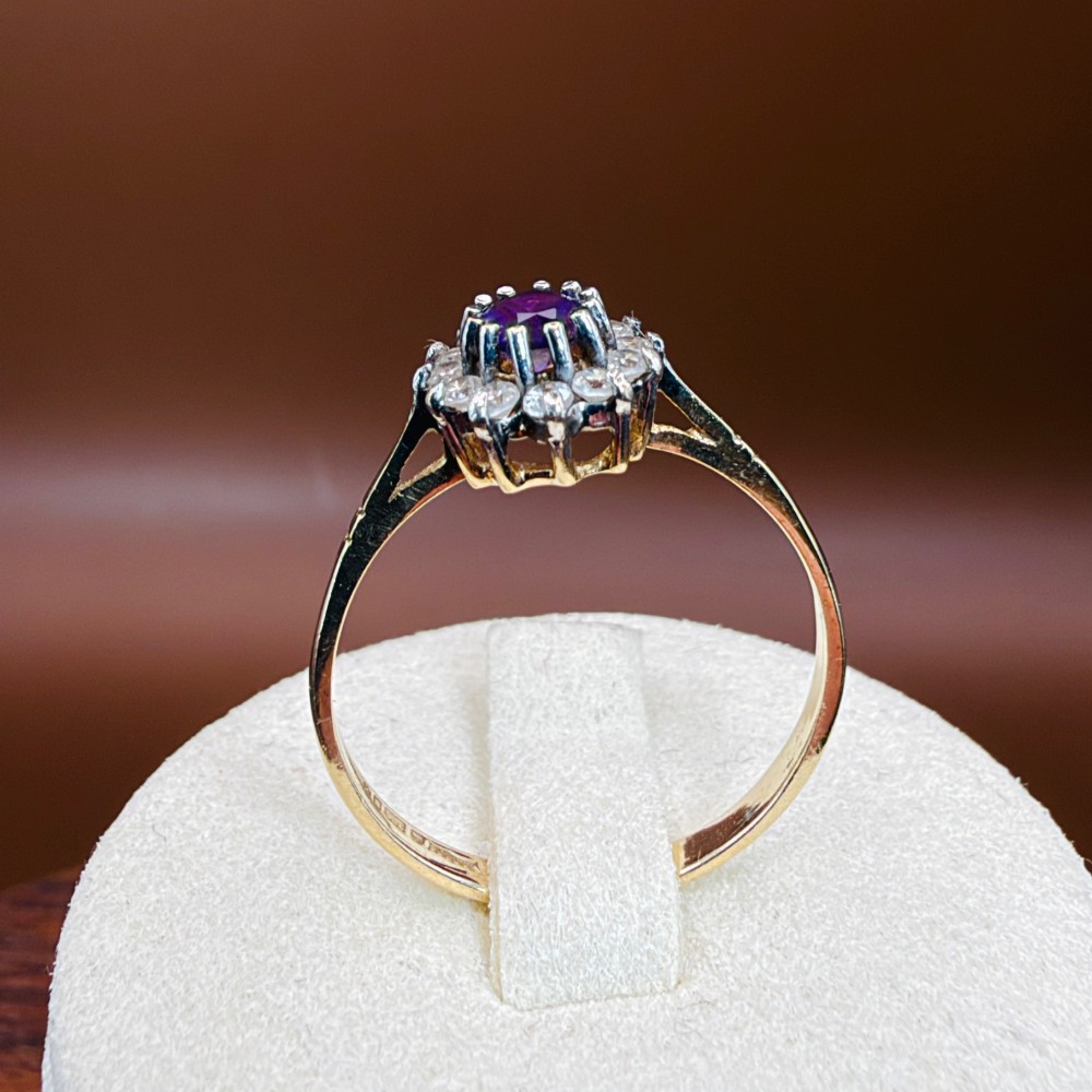 A vintage 9ct yellow gold ring featuring a central oval purple amethyst framed by a halo cluster of round white spinel gemstones. View XIII