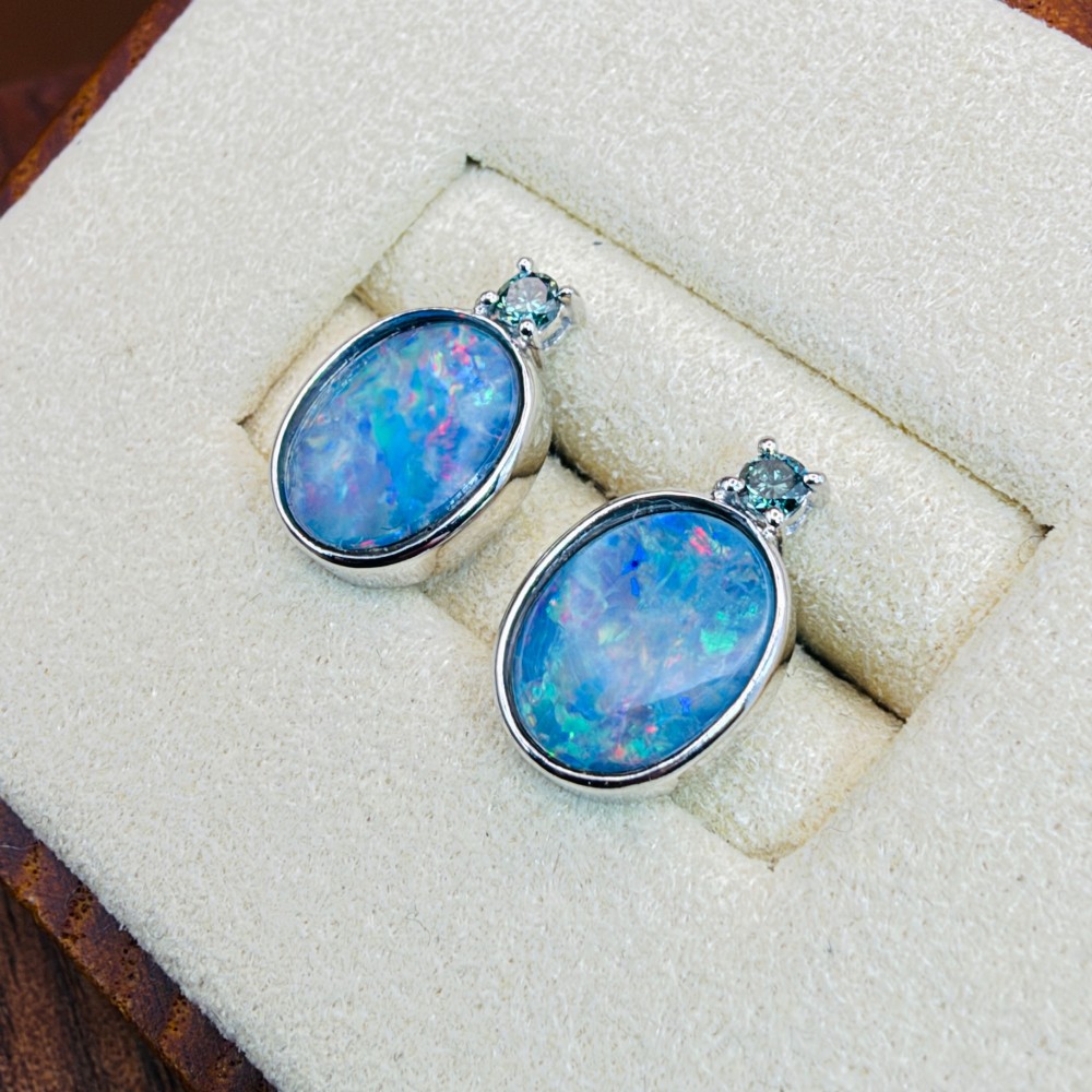 A pair of 14ct white gold stud earrings featuring oval opal doublets with blue and green flashes, each crowned with a small round prong-set teal green diamond. View III