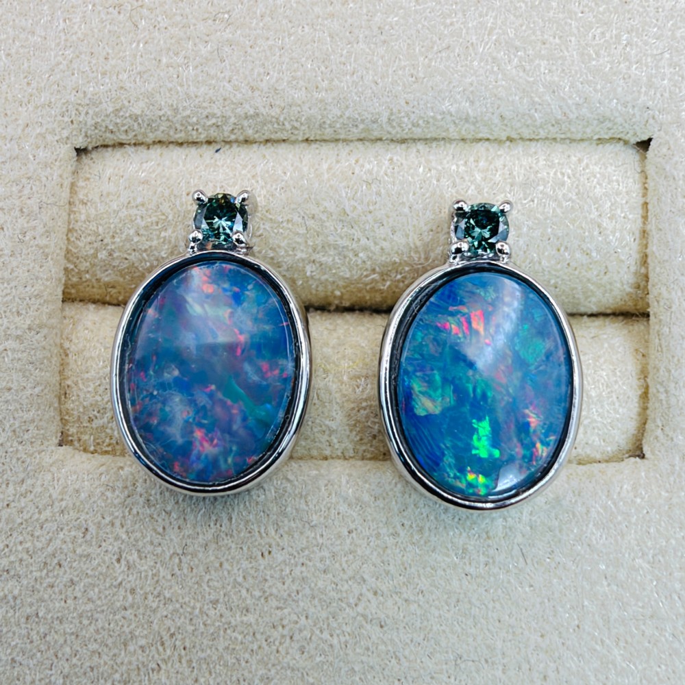 A pair of 14ct white gold stud earrings featuring oval opal doublets with blue and green flashes, each crowned with a small round prong-set teal green diamond. View V