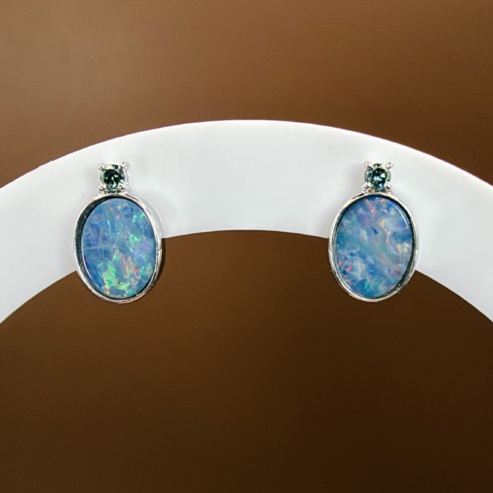 A pair of 14ct white gold stud earrings featuring oval opal doublets with blue and green flashes, each crowned with a small round prong-set teal green diamond. View VI