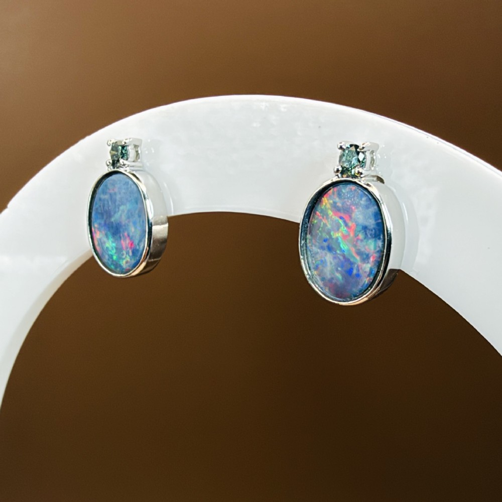 A pair of 14ct white gold stud earrings featuring oval opal doublets with blue and green flashes, each crowned with a small round prong-set teal green diamond. View VII