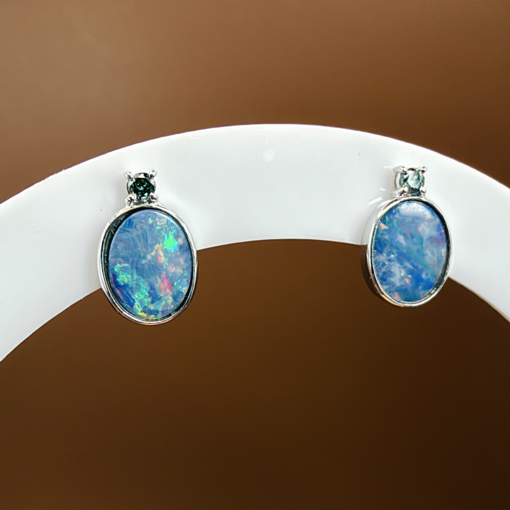 A pair of 14ct white gold stud earrings featuring oval opal doublets with blue and green flashes, each crowned with a small round prong-set teal green diamond. View VIII