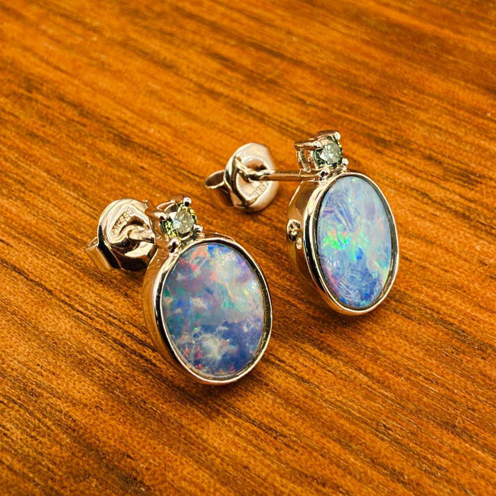 A pair of 14ct white gold stud earrings featuring oval opal doublets with blue and green flashes, each crowned with a small round prong-set teal green diamond. View XI