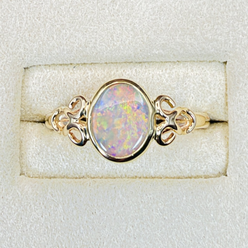 An 18ct gold ring featuring a central oval bezel-set opal displaying colourful flash, flanked by openwork scrolled shoulders. View II