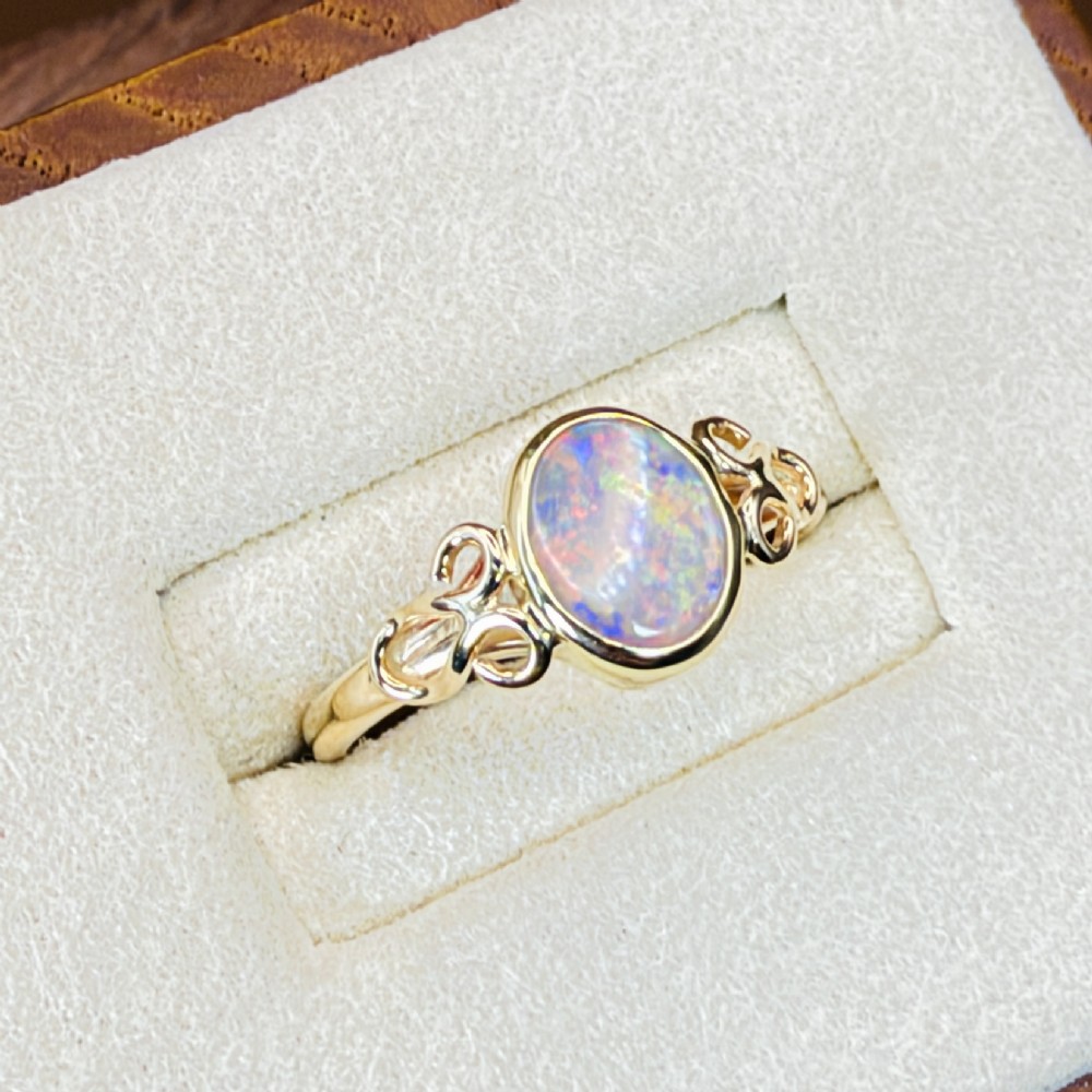 An 18ct gold ring featuring a central oval bezel-set opal displaying colourful flash, flanked by openwork scrolled shoulders. View VI