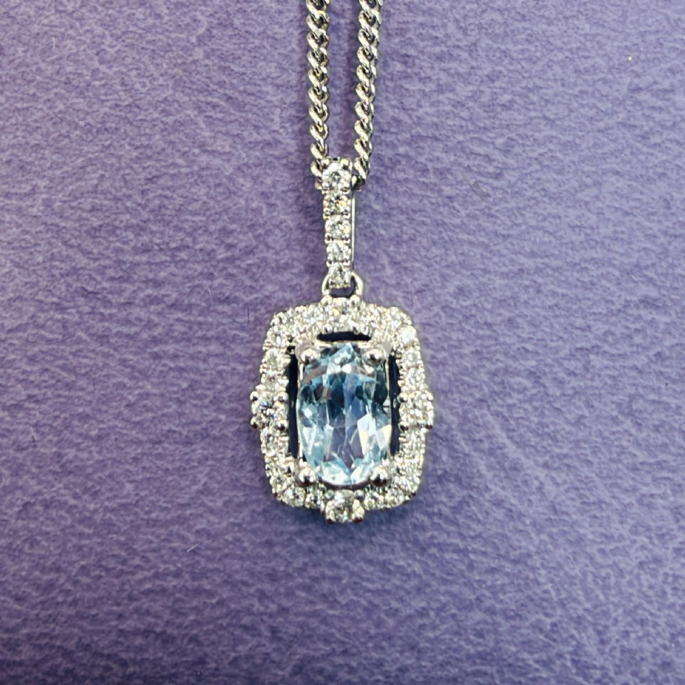 An 18ct white gold pendant featuring a central oval-cut light blue aquamarine surrounded by a frame of round brilliant diamonds with a diamond-set bail. View II