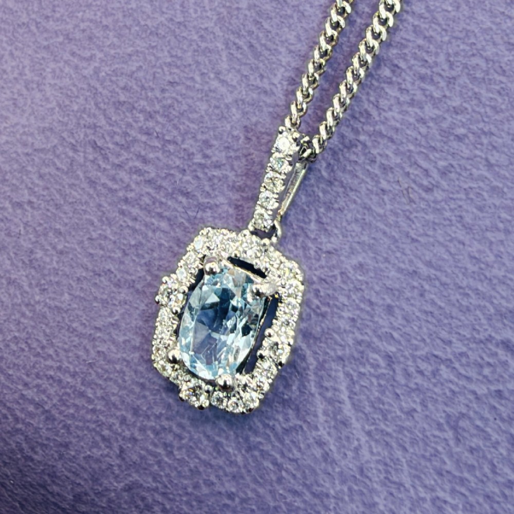 An 18ct white gold pendant featuring a central oval-cut light blue aquamarine surrounded by a frame of round brilliant diamonds with a diamond-set bail. View III
