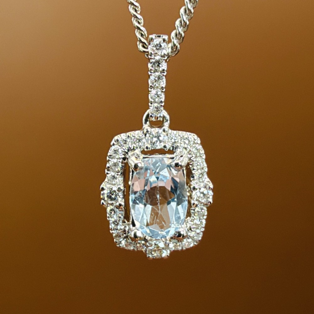 An 18ct white gold pendant featuring a central oval-cut light blue aquamarine surrounded by a frame of round brilliant diamonds with a diamond-set bail. View VII