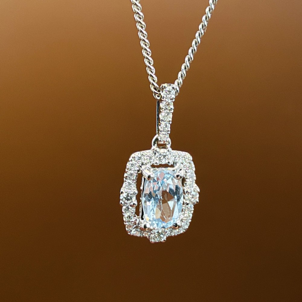 An 18ct white gold pendant featuring a central oval-cut light blue aquamarine surrounded by a frame of round brilliant diamonds with a diamond-set bail. View VIII
