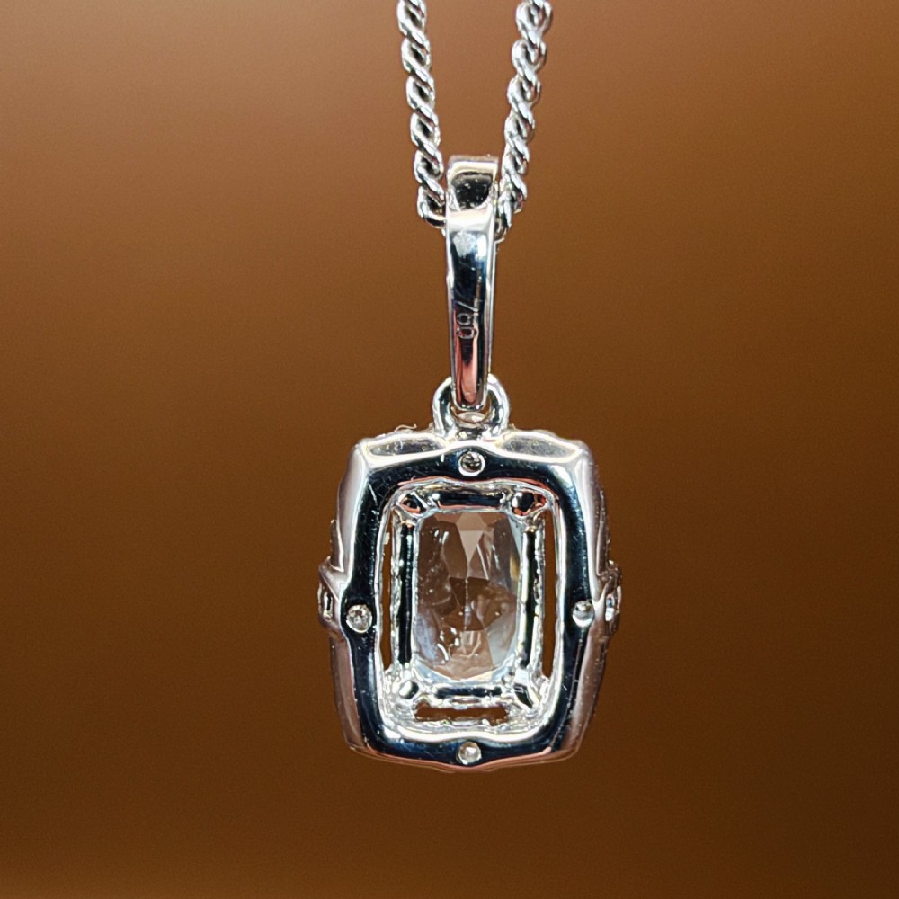 An 18ct white gold pendant featuring a central oval-cut light blue aquamarine surrounded by a frame of round brilliant diamonds with a diamond-set bail. View IX