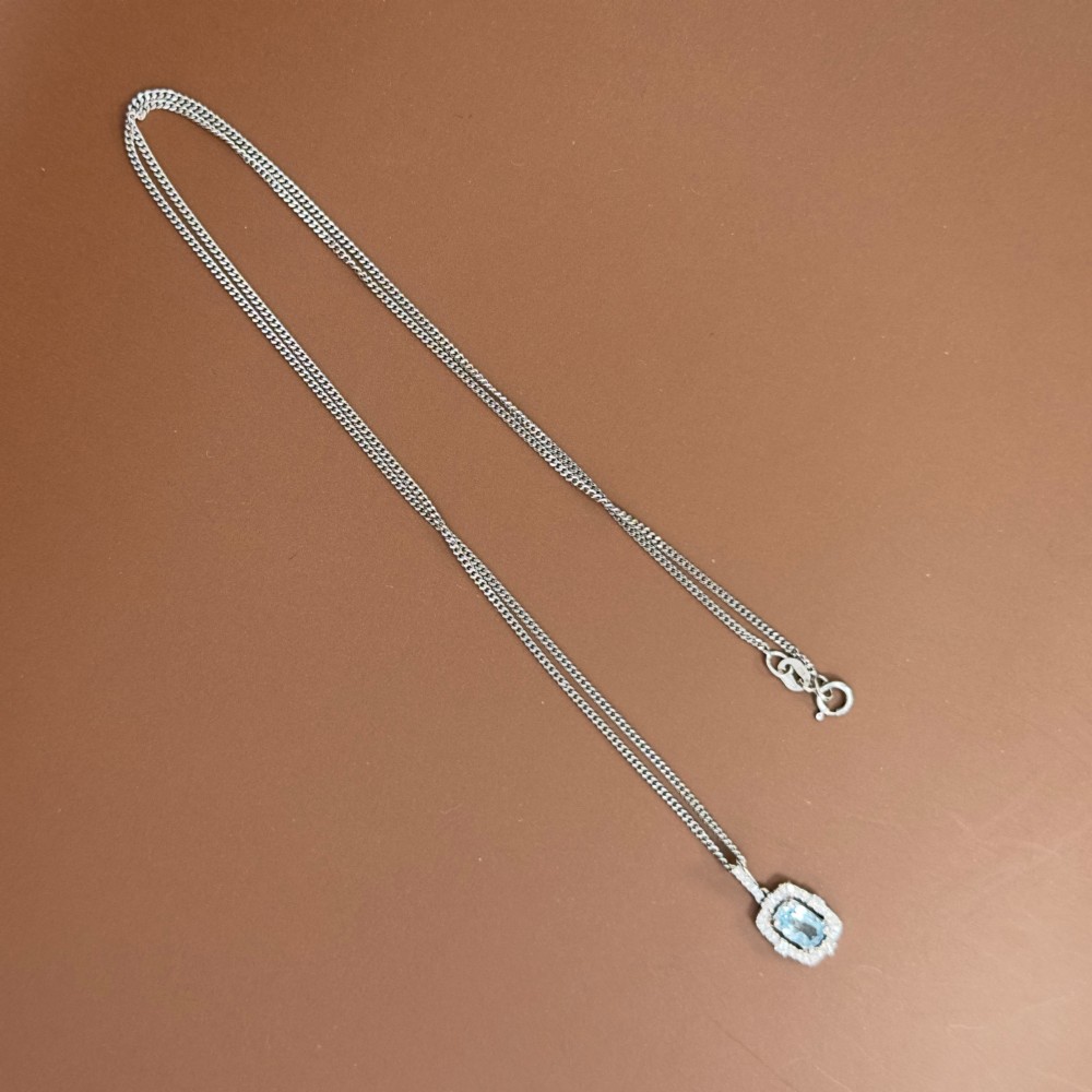 An 18ct white gold pendant featuring a central oval-cut light blue aquamarine surrounded by a frame of round brilliant diamonds with a diamond-set bail. View XIV