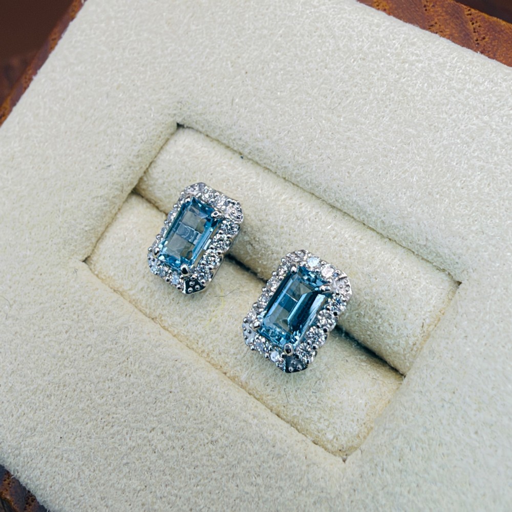 A pair of platinum stud earrings featuring emerald-cut light blue aquamarines surrounded by a border of brilliant-cut diamonds. View II