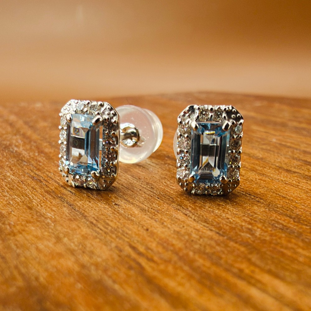 A pair of platinum stud earrings featuring emerald-cut light blue aquamarines surrounded by a border of brilliant-cut diamonds. View V