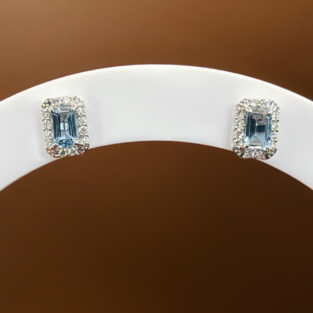 A pair of platinum stud earrings featuring emerald-cut light blue aquamarines surrounded by a border of brilliant-cut diamonds. View IX