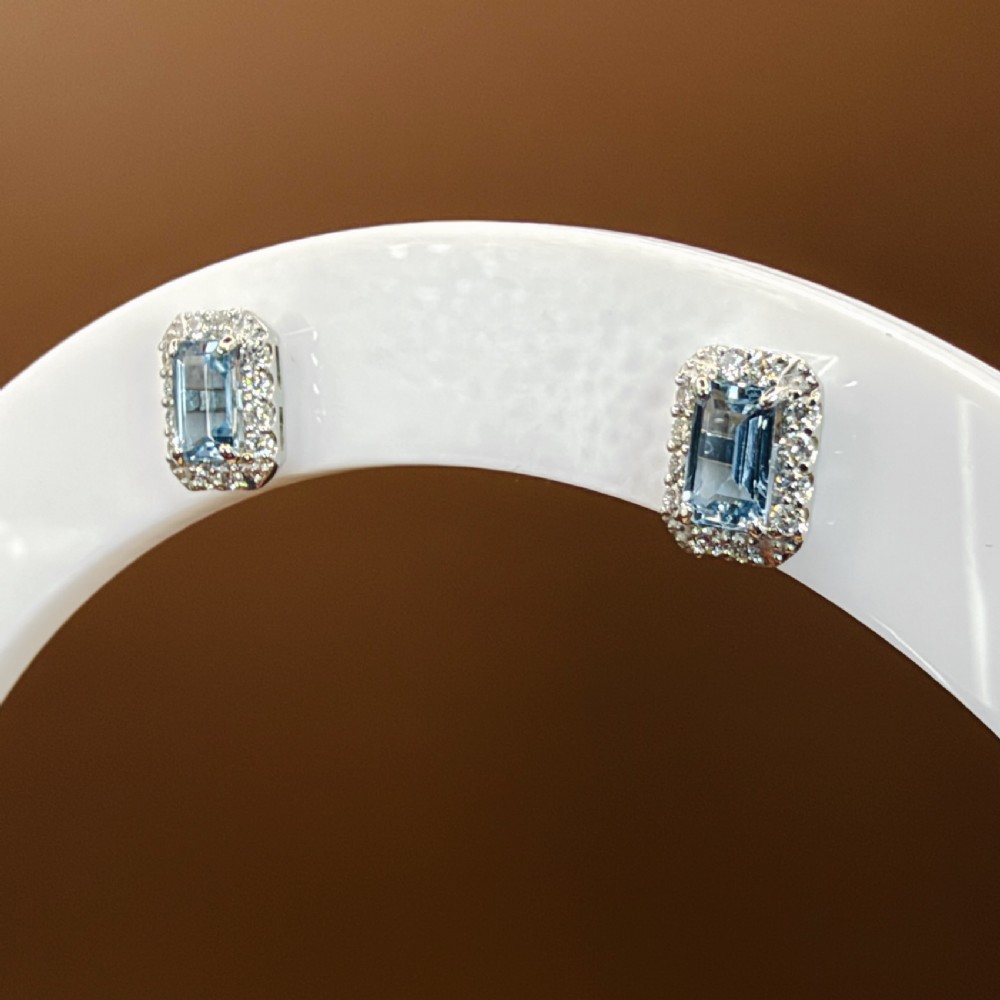 A pair of platinum stud earrings featuring emerald-cut light blue aquamarines surrounded by a border of brilliant-cut diamonds. View X