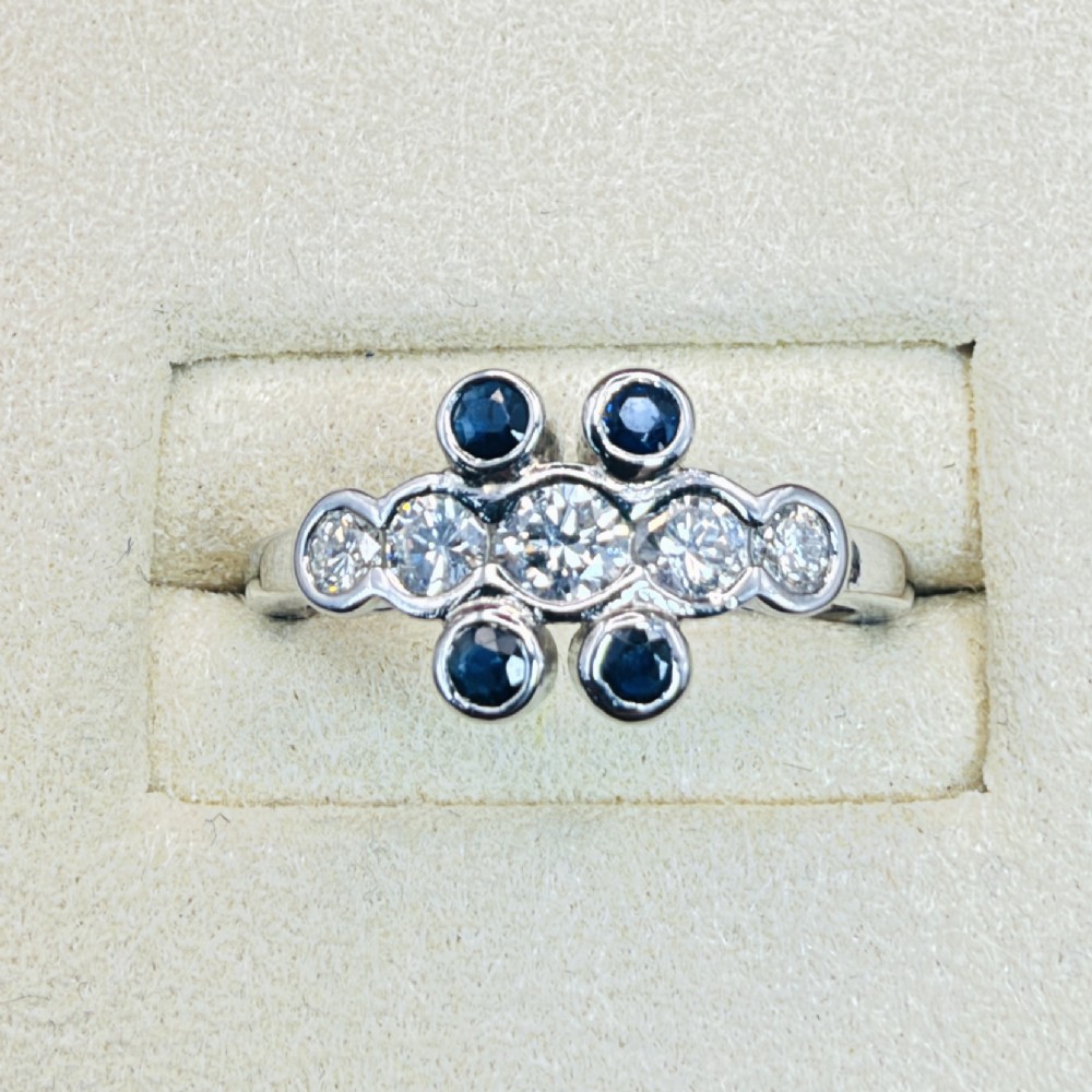 A platinum ring crafted with five bezel-set diamonds in a central horizontal row, flanked by four small round blue sapphires. View II