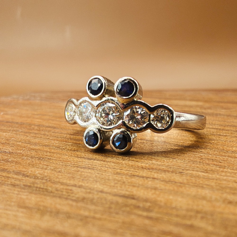 A platinum ring crafted with five bezel-set diamonds in a central horizontal row, flanked by four small round blue sapphires. View VI