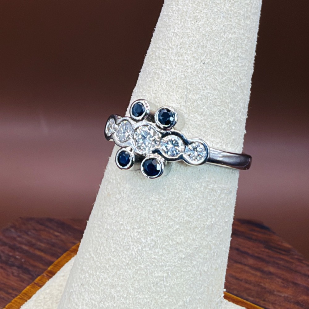 A platinum ring crafted with five bezel-set diamonds in a central horizontal row, flanked by four small round blue sapphires. View X