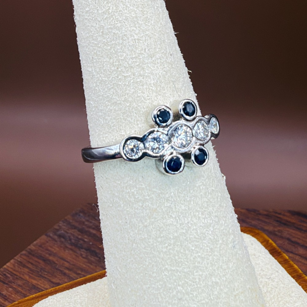 A platinum ring crafted with five bezel-set diamonds in a central horizontal row, flanked by four small round blue sapphires. View XI