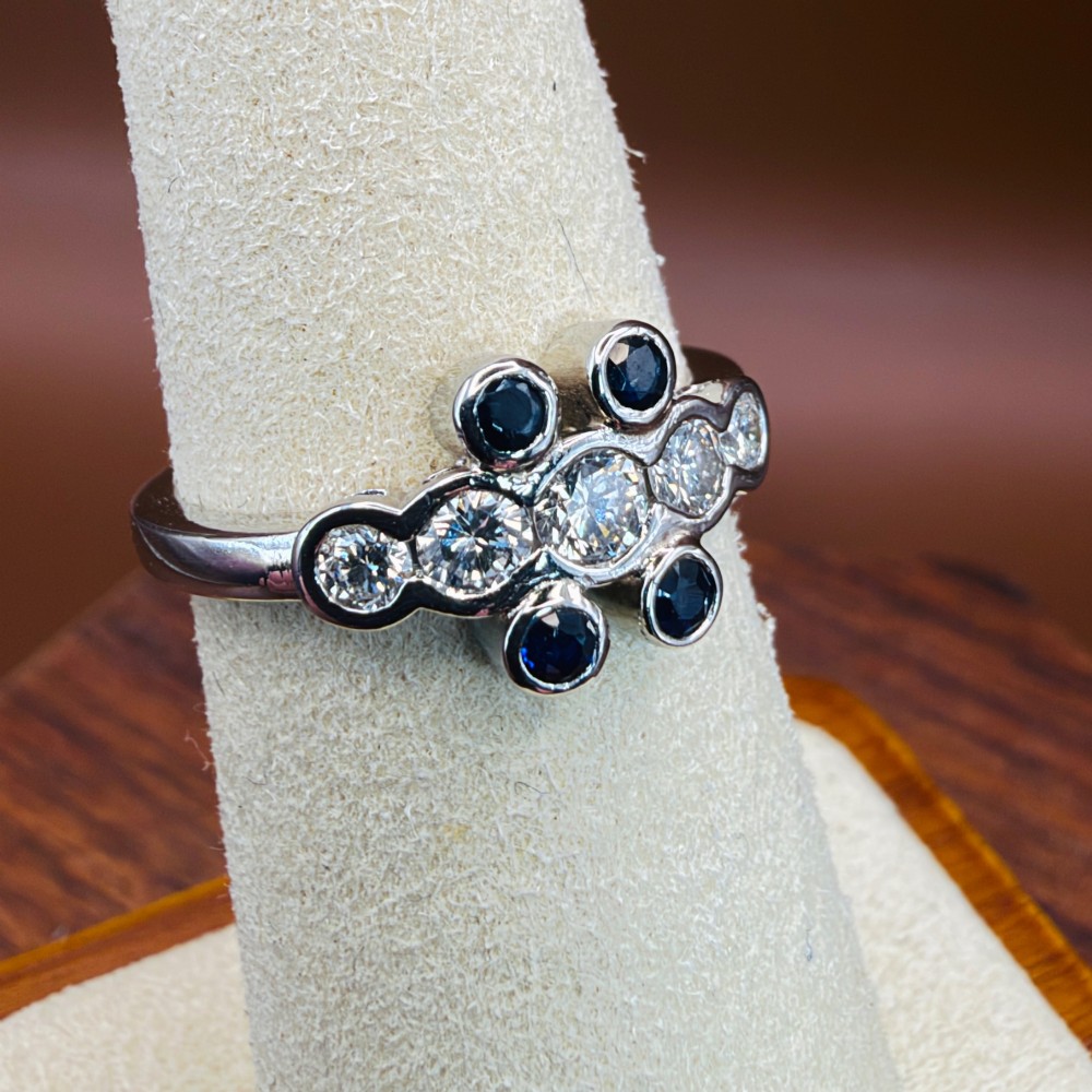 A platinum ring crafted with five bezel-set diamonds in a central horizontal row, flanked by four small round blue sapphires. View XII