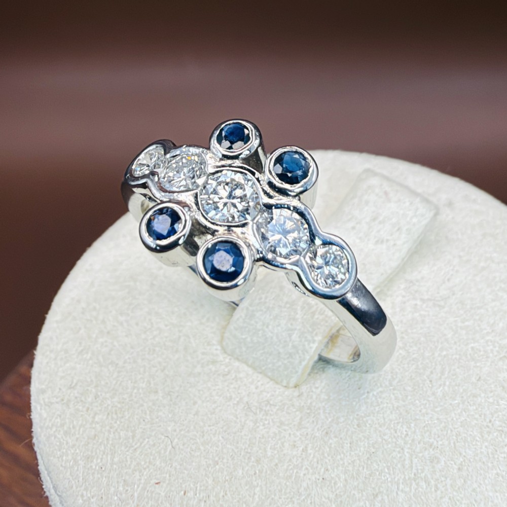 A platinum ring crafted with five bezel-set diamonds in a central horizontal row, flanked by four small round blue sapphires. View XIII