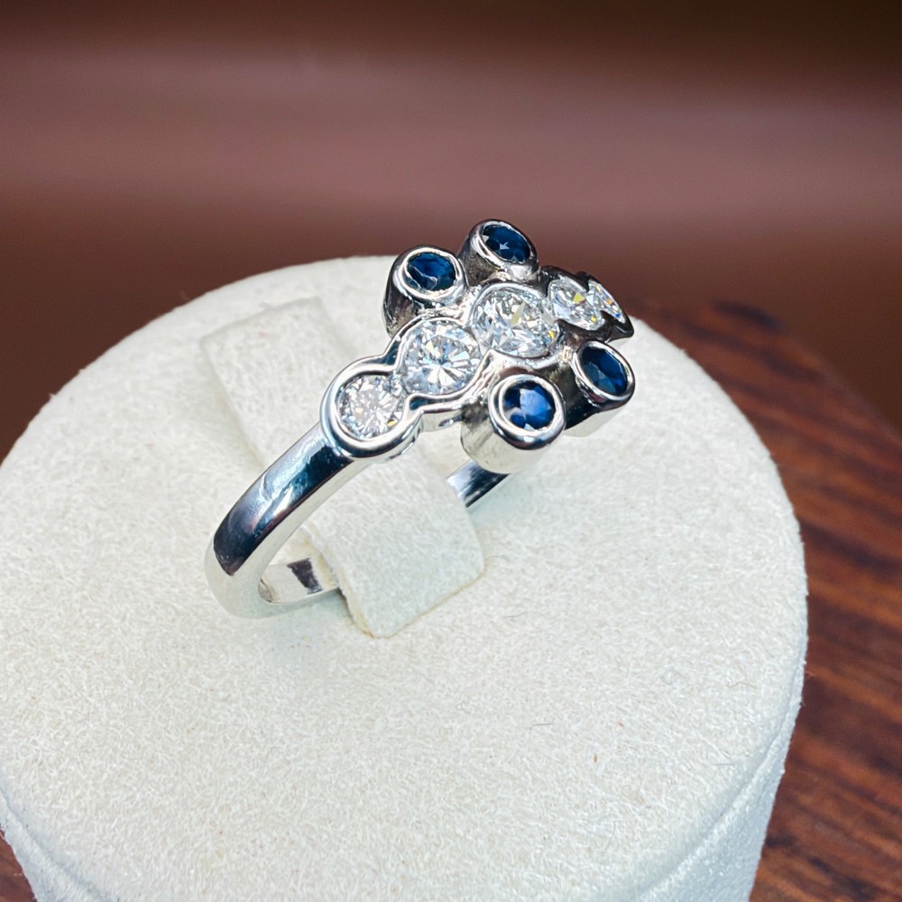 A platinum ring crafted with five bezel-set diamonds in a central horizontal row, flanked by four small round blue sapphires. View XIV