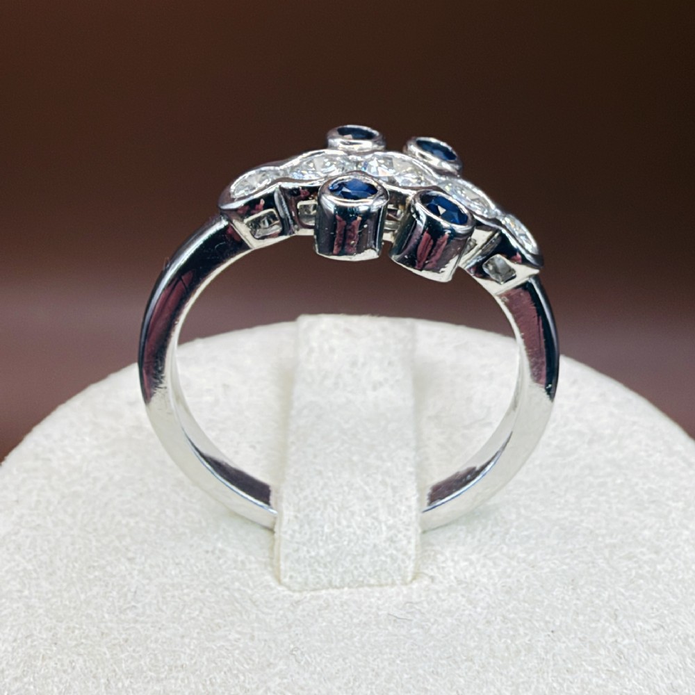 A platinum ring crafted with five bezel-set diamonds in a central horizontal row, flanked by four small round blue sapphires. View XV