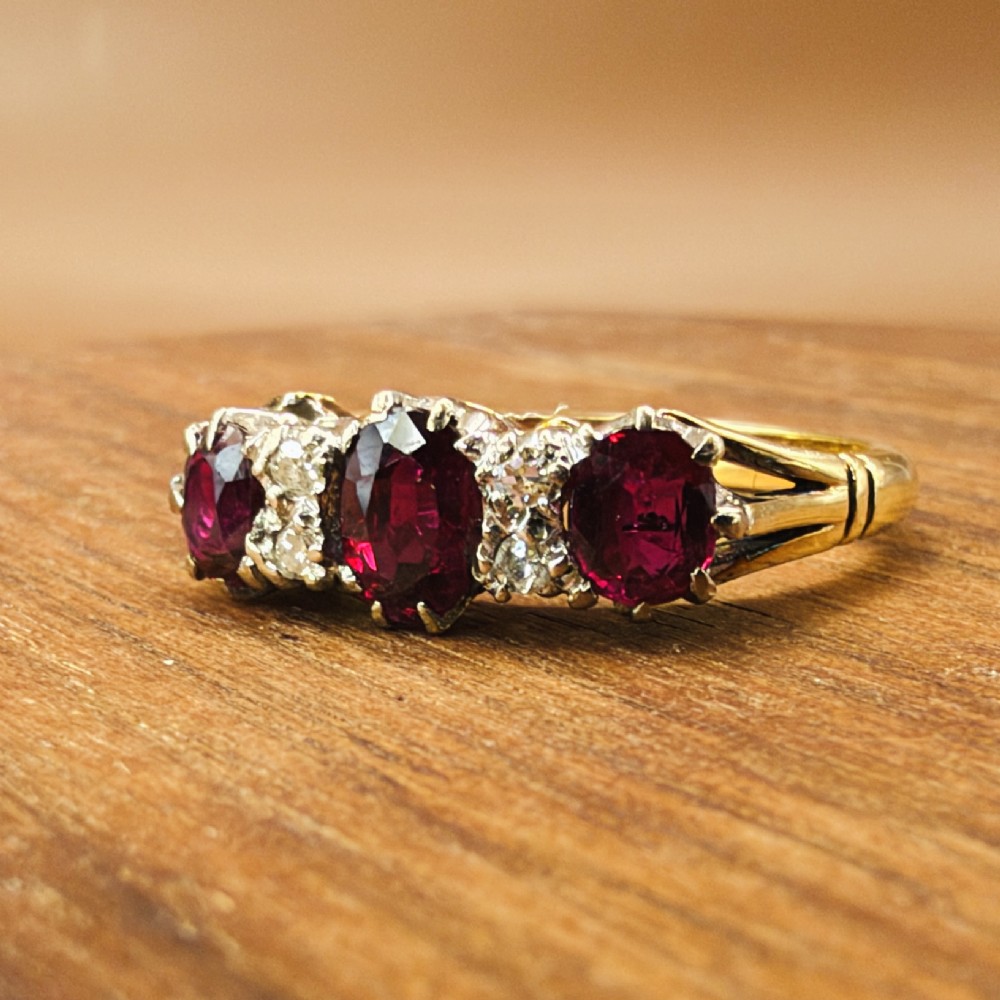 An 18ct yellow gold ring featuring three oval red rubies separated by pairs of small diamonds set in a claw setting. View VI