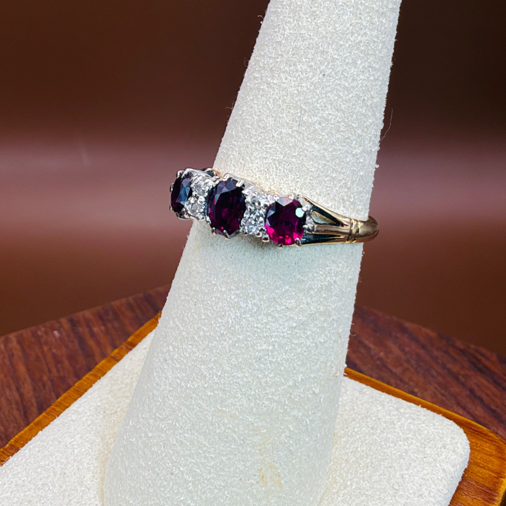 An 18ct yellow gold ring featuring three oval red rubies separated by pairs of small diamonds set in a claw setting. View IX