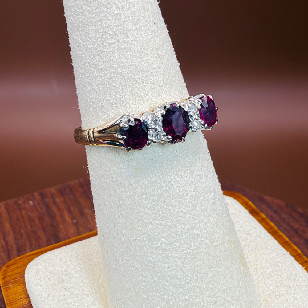 An 18ct yellow gold ring featuring three oval red rubies separated by pairs of small diamonds set in a claw setting. View X
