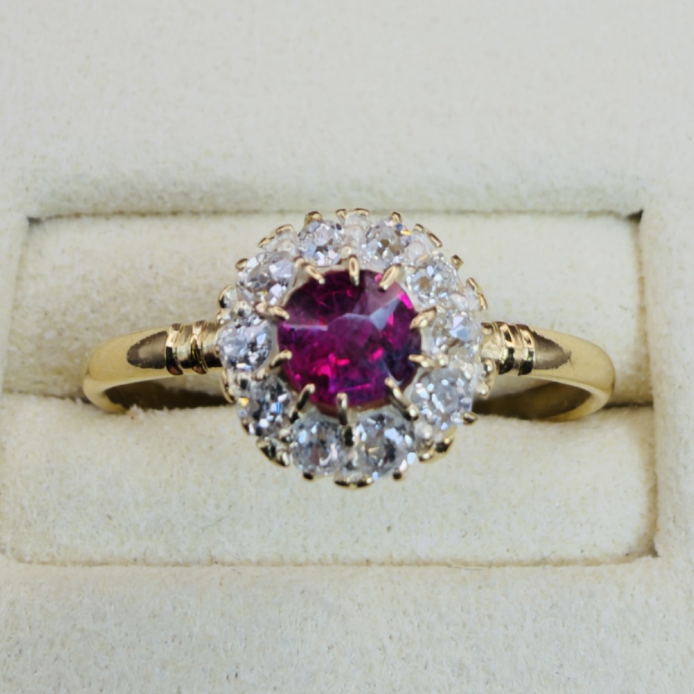 An 18ct yellow gold Victorian ring featuring a central round red ruby surrounded by a halo of hand-cut diamonds. View V